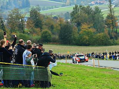 Zuschauer bei einer Rallyeveranstaltung, im Hintergrund ein Rallyeauto (Symbolbild)